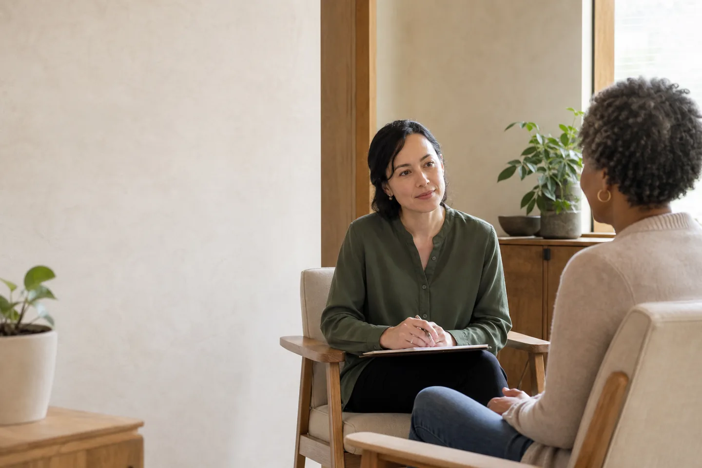 A clinician listens attentively to a patient during a calm consultation in a warm daylight room.